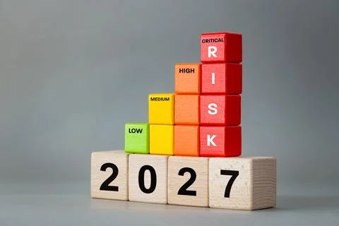 Tower of red blocks with word RISK stacked on wooden cubes with year 2027  Stock-Fotos