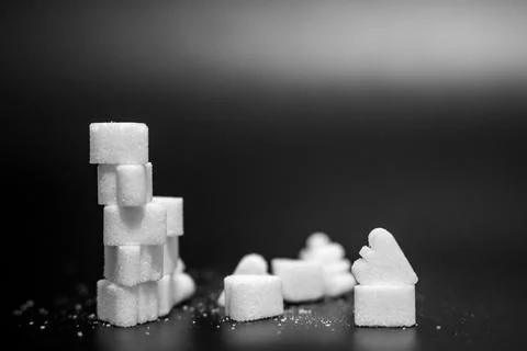 Tower of white sugar cubes beside scattered heart shaped sugar pieces on a black Stock Photos