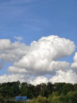 Towering cumulus clouds over forest with roadside direction signs and blue sk Stock Photos