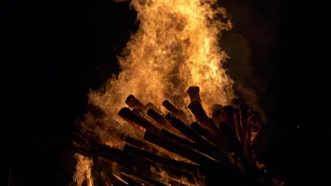 Towering flames engulf stacked logs in a dramatic fiery display. Slow motion Stock Footage 308661712