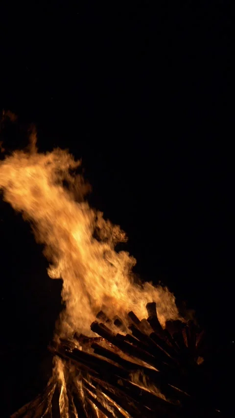 Towering flames rise into the night sky, fueled by a large stack of wooden logs Stock Footage 316420383
