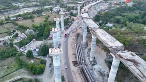Towering flyover columns dwarfing rural landscape and highway. Stockbeeldmateriaal 335168172