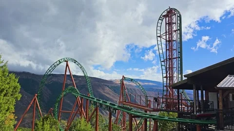 A towering mountain roller coaster rises above a canyon, with green rails Stock Footage 345250040