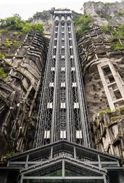 A towering multi-shaft glass elevator climbing vertically against a majesti.. Stock Photos
