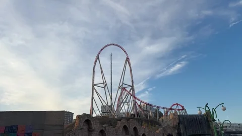 A towering red-and-white roller coaster rises above rocky structures Stock Footage 321340791