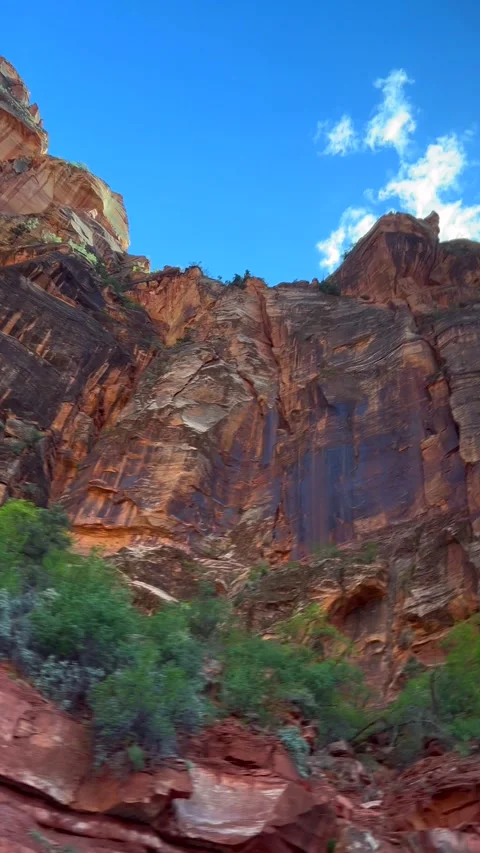 Towering red rock cliff rises under bright sky with scattered clouds. Texture Stock Footage 314307291