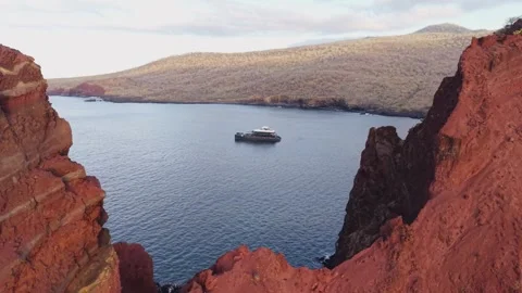 Towering red volcanic cliffs overlooking tourist yacht gliding through crystal Stock-Footage 308391495