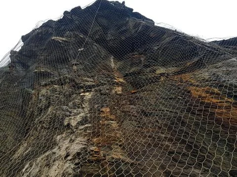 A towering rock face is covered with protective netting to mitigate the risk  Stock Photos