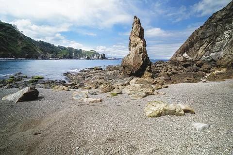 Towering sea stack on pebbled beach with coastline Stock Photos