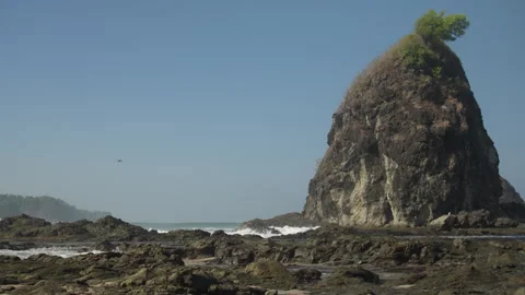Towering Sea Stack on a Rocky Coast with Waves Crashing Below Stock Footage 338300449