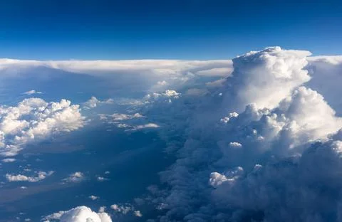 Towering sunlit cloud rising above cloudscape during high altitude flight Stock Photos