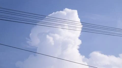 Towering White Cumulus Cloud Behind Overhead Power Lines In Blue Sky Stock Photos