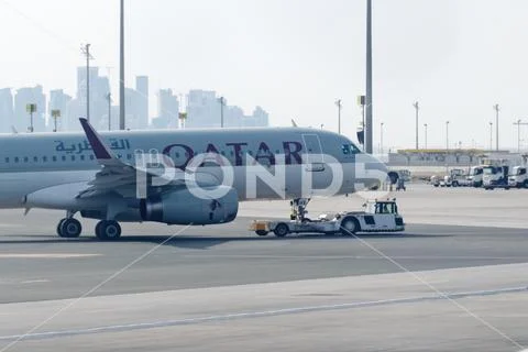Towing tractor pushing airplane by Qatar airline on Doha airport Stock Photos
