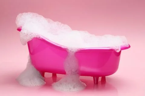 Toy bathtub overflowing with foam on pink background Stock Photos