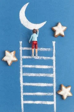 A toy boy is climbing to the moon using a ladder made from sugar powder on blue Fotos Stock