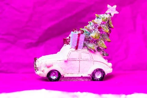 Toy car, Christmas tree gifts on roof on a pink background. Happy 2022 New Year. Stock Photos