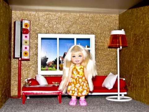 Toy doll on a sofa in a room with a window and a lamp Stock Photos