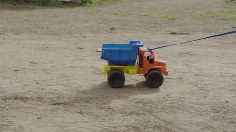 Toy dump truck being pulled by a cord on dirt ground Stock Footage 314065241