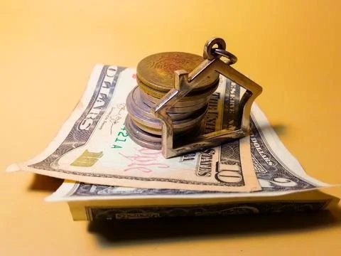 A toy house next to a stack of coins and American dollars and a key Foto stock