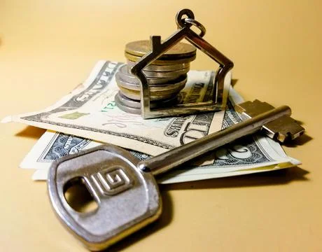 A toy house next to a stack of coins and American dollars and a key Foto stock