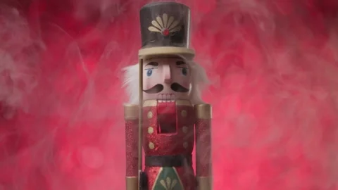 Toy Nutcracker standing on red bokeh background, surrounded by smoke, beautiful Stock Footage 321679396