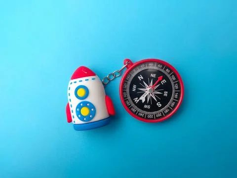 A toy rocket keychain is attached to a red magnetic navigation compass over.. Stock-Fotos