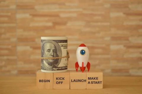 Toy rocket, money banknote with phrase BEGIN, KICK OFF, LAUNCH and MAKE A STA Stock-Fotos
