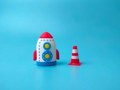 A toy rocket placed beside a small red and white traffic cone on a blue bac.. Stock Photos