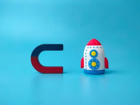 A toy rocket positioned next to a blue and red horseshoe magnet on a blue s.. Stock Photos