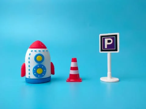 A toy rocket, a red traffic cone, and a parking sign stand arranged in a ro.. Stock Photos