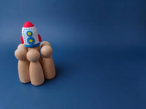 A toy rocket sits perched on top of a cluster of wooden peg figures against.. Stock Photos