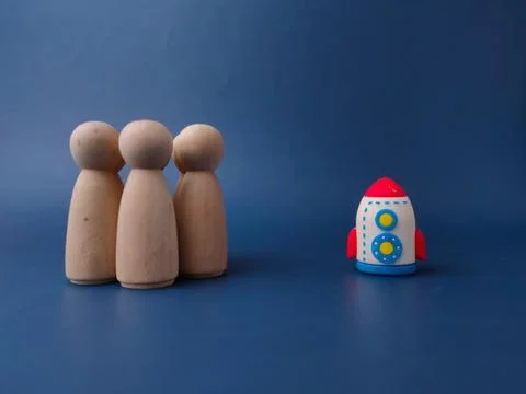 A toy rocket stands positioned at a distance from a group of wooden peg fig.. Stock Photos