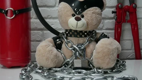Toy Teddy bear dressed in leather belts and a mask chained and locked with a Stock Footage 142886985