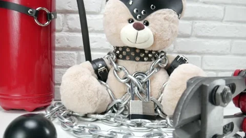 Toy Teddy bear dressed in leather belts and a mask chained and locked with a Stock Footage 142887012