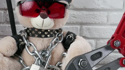 Toy Teddy bear dressed in leather belts and a mask chained and locked with a Stock Footage 142887044