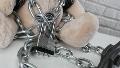 Toy Teddy bear dressed in leather belts and a mask chained and locked with a Stock Footage 142887086