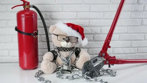 A toy Teddy bear dressed in leather belts and a Santa Claus hat is chained and Stock Footage 143455864