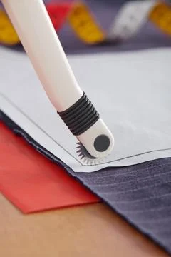 Tracing wheel on sewing pattern, red transfer paper under fabric, sewing eq.. Stock-Fotos