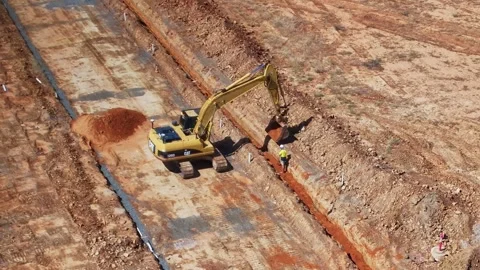 Track loader operator dropping soil into a trench under direction of worker Stock Footage 266475516