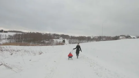 Track shot mom and son sledding on snow covered road on cold winter day Stock Footage 122496523