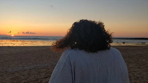 Track shot of a woman while walking in the beach from back at sunset. Video stock 111978005