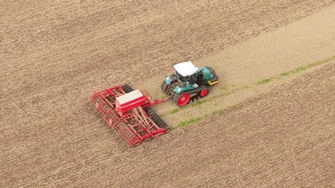 Tracked farm tractor pulling wide seed drill across cultivated soil. Crop sowing Stock Footage 345501164