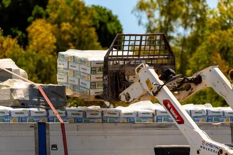 Tracked loader unloading palletized bags from truck platform Photos