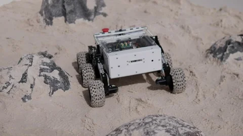 Tracked robotic rover climbing over sandy rock terrain with white body, clear Stock Footage 344876051