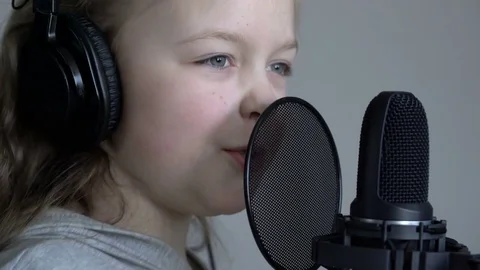 Tracking close-up shot of Cute little blonde girl with headphones singing with a Video stock 75172956