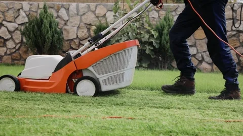 Tracking close up shot of a man mows the grass in the backyard with a lawn mower Stock Footage 164873572