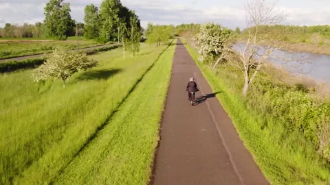 Tracking drone shot of a man riding his bike next to river Stock Footage 194446624