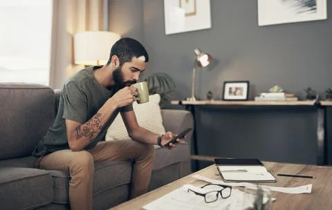 Tracking his spending with smart apps. a young man having coffee and using a Stock Photos