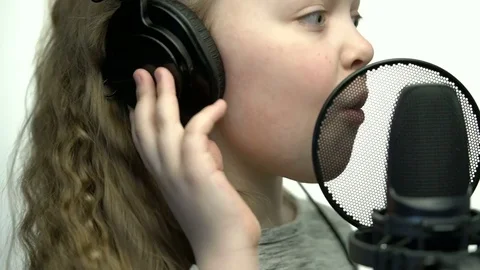 Tracking medium close-up shot of cute little blonde girl with headphones singing Stock Footage 75177813