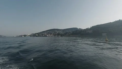 Tracking over sunlit water toward Adalar's hazy hillside coast Stock Footage 320029356